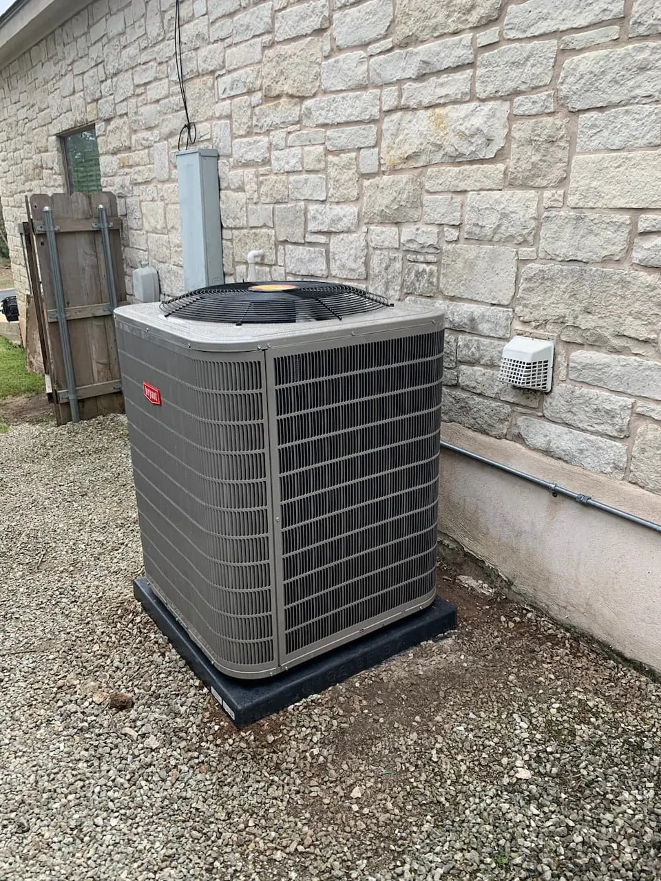 New outdoor AC condenser installed beside a stone home